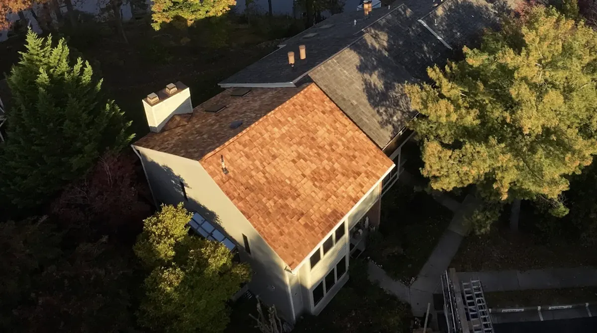 Aerial view of a two-story house with a reddish-brown wood shake roof section next to gray shingle roof sections and a white chimney