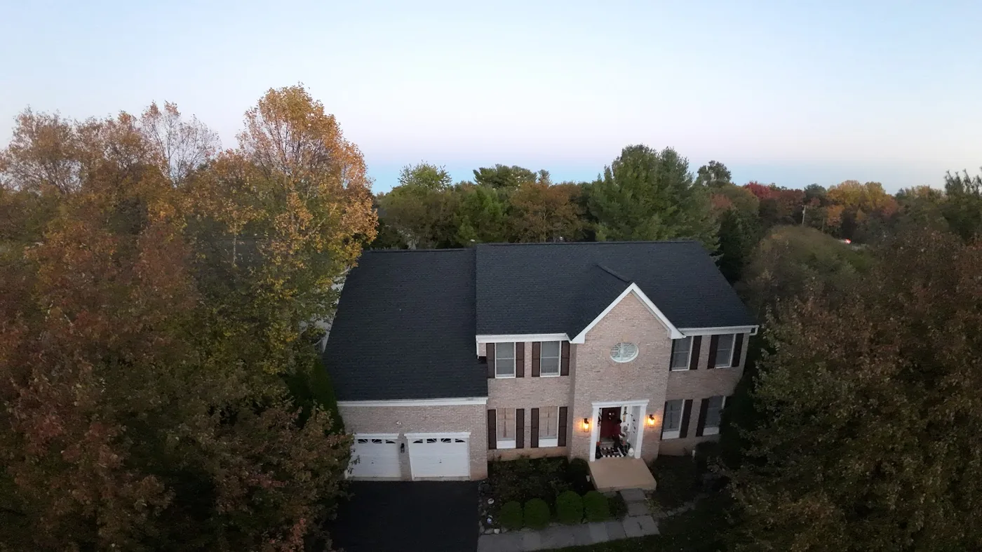 Dark shingle roof on a two-story brick house with a front-facing gable, surrounded by trees in fall color