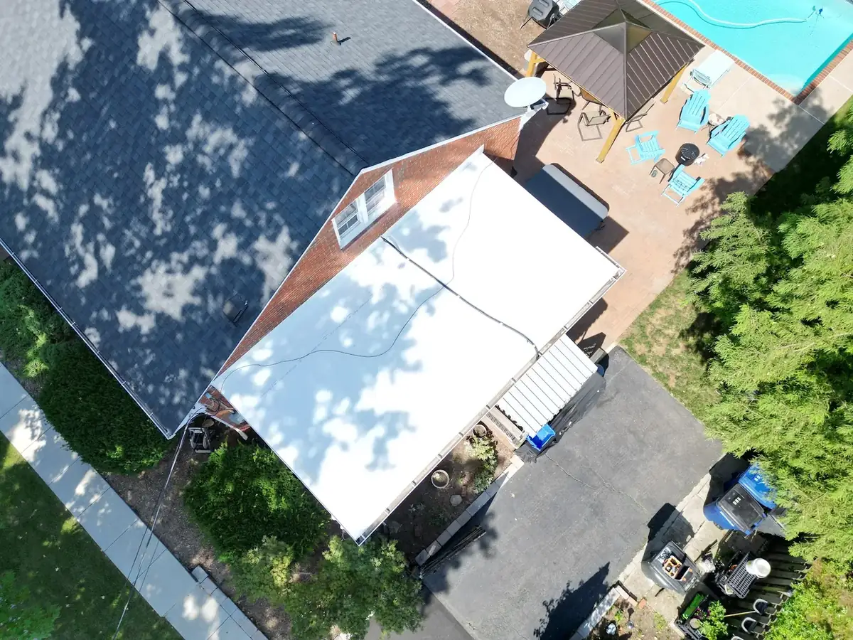 Aerial view of a white flat membrane roof section beside a dark shingle roof and a backyard patio